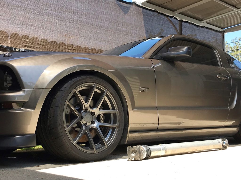 ford mustang with one piece performance driveshaft laying alongside it on the ground
