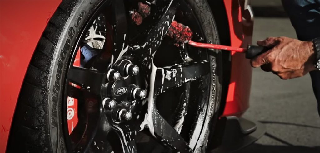man cleaning a custom wheel on a fancy car