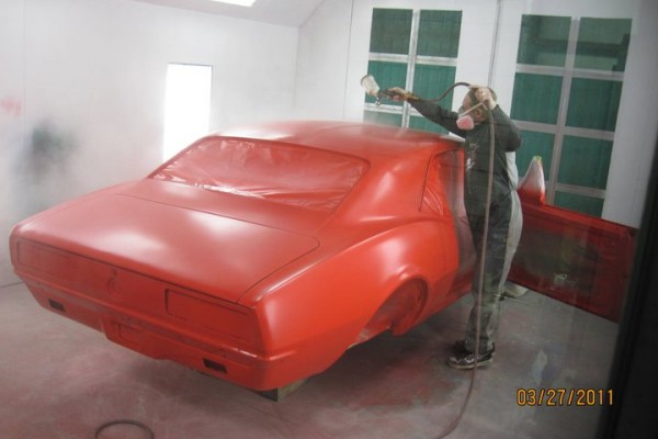 man spraying paint onto a vintage 1967 chevy camaro in a spray booth