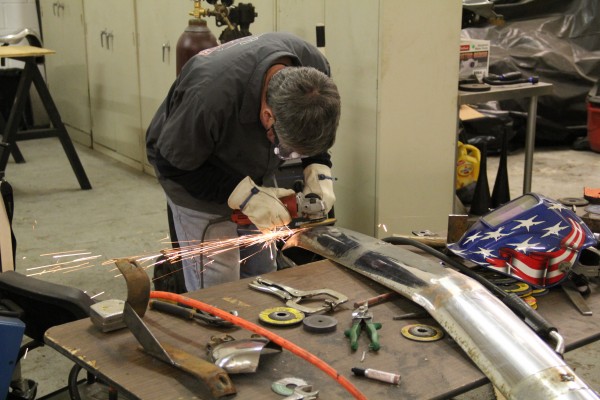 man grinding metal on an old car bumper