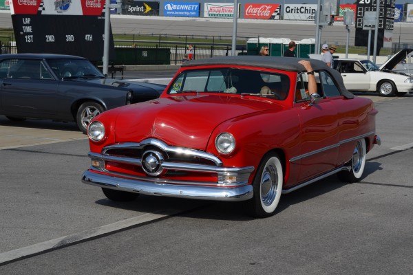 man driving a red convertible shoebox ford