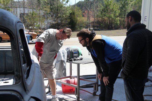 men examining a bare metal hot rod body prior to paint