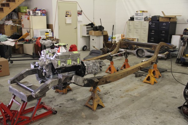 bare frame of a vintage car with v8 engine mounted during a hot rod build