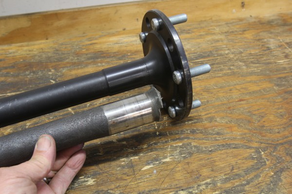 man holding a broken damaged axle next to a new replacement one