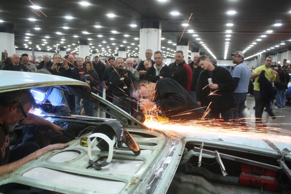 man using a cutting wheel on an old car fender during car show demonstration