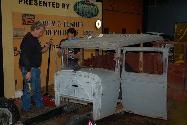 men chopping and lowering a hot rod roof and body onto a frame