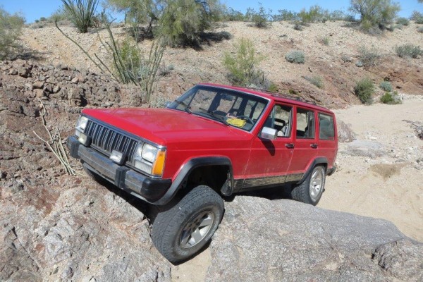 a jeep cherokee xj crawling over rocks and boulders in a desert