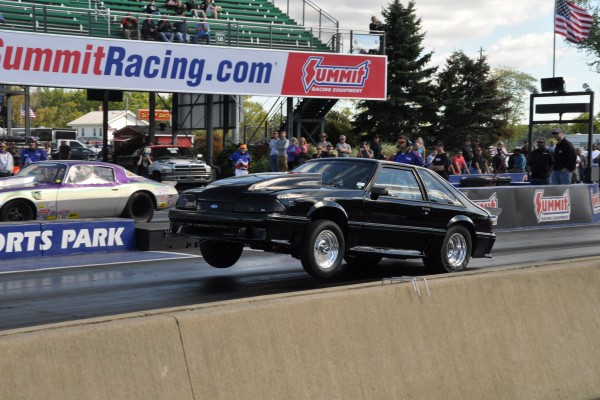 fox body musclecar doing a wheelstand at a dragstrip
