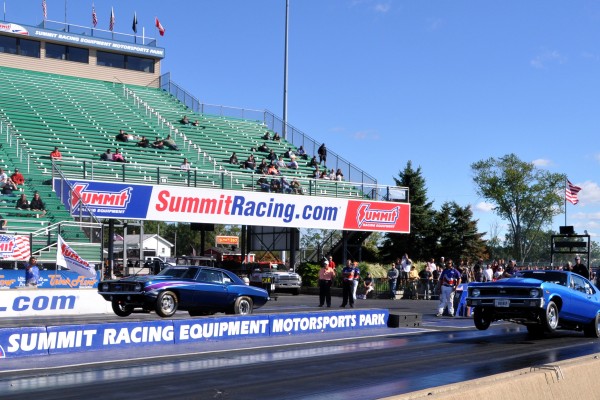 a vintage chevy nova and camaro doing wheelstands at dragstrip