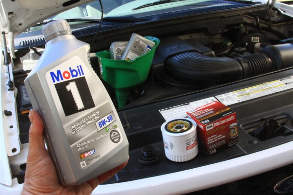 man holding a jug of motor oil near an engine
