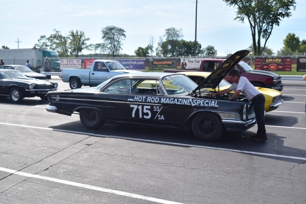 man in staging lanes of a drag race working on his car