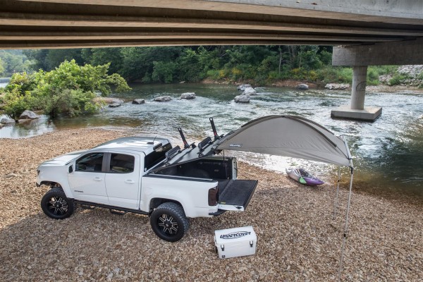 truck with tonneau cover, bed rack, and awning deployed near a river