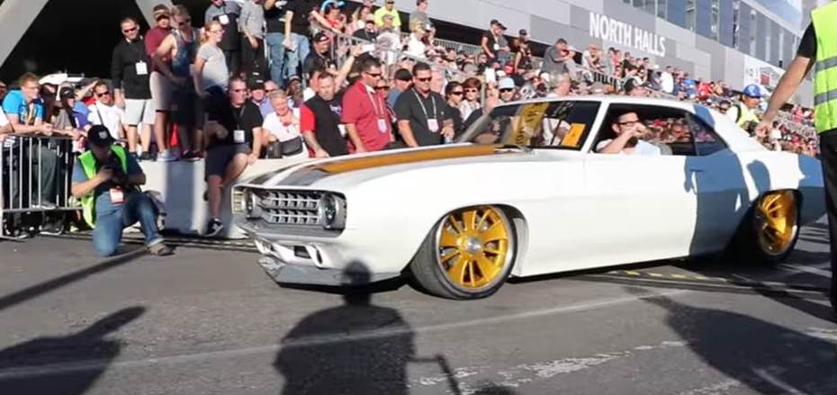 white 1969 chevy camaro driving in parade with crowd