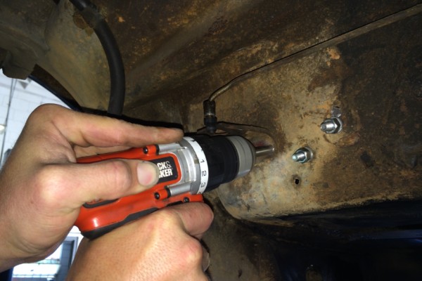 man drilling holes into chassis of 1968 ford mustang