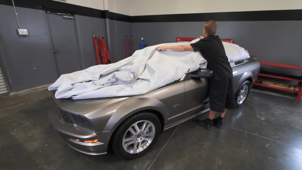 man covering late model ford mustang with protective car dust cover
