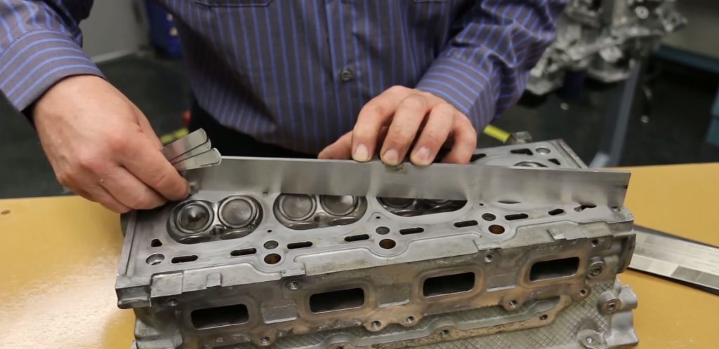 man using straight edge to determine flatness on an engine cylinder head