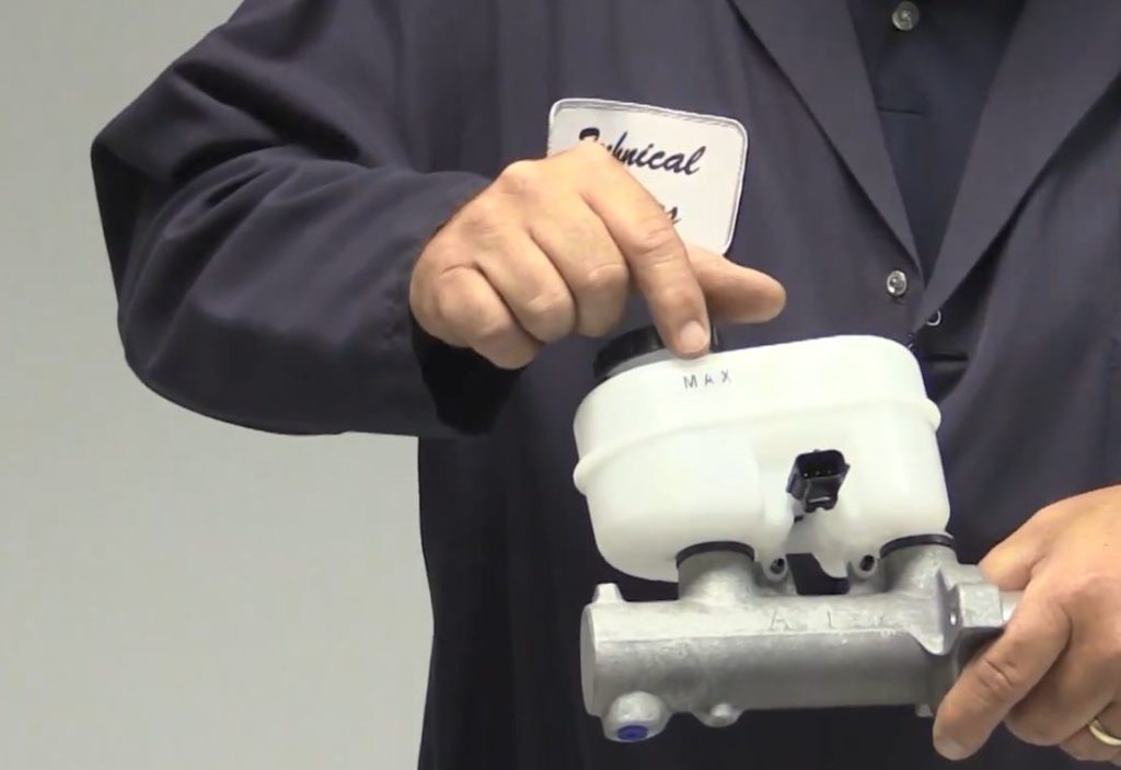 man pointing to a master cylinder brake fluid reservoir