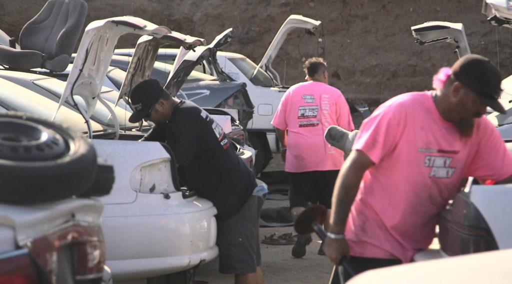 men scavenging in a junkyard for car parts