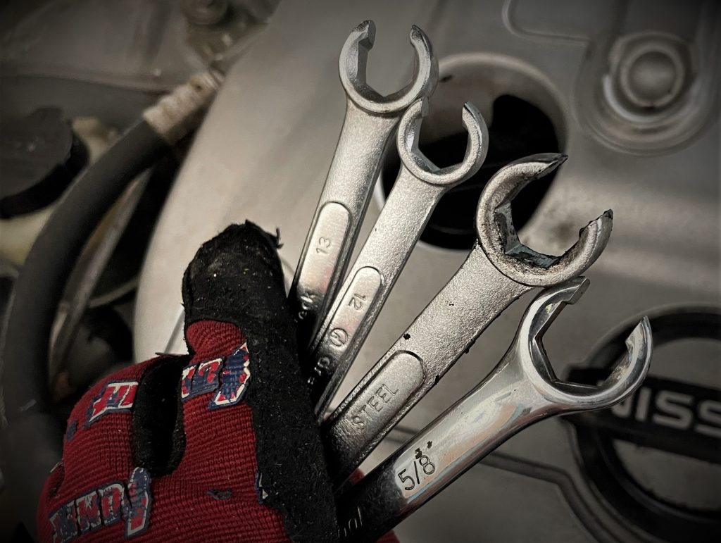 gloved hand holding flare wrenches near an engine