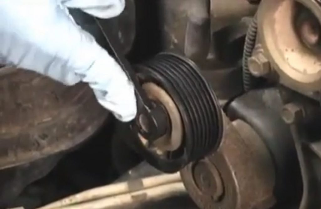 close up of a man tightening a pulley on an engine