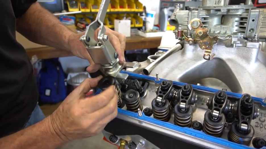 man removing valve springs from a cylinder head using a compressor tool