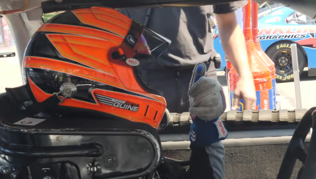 man in a race car with helmet giving a thumbs up