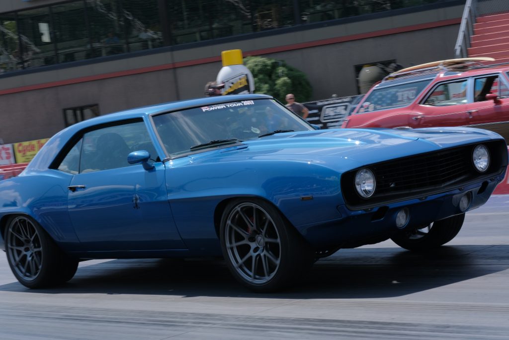 blue chevy camaro dragster races an oldsmobile vista cruiser at a dragstrip