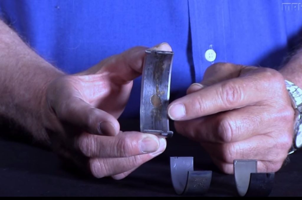 man showing inside of worn engine crank main bearing