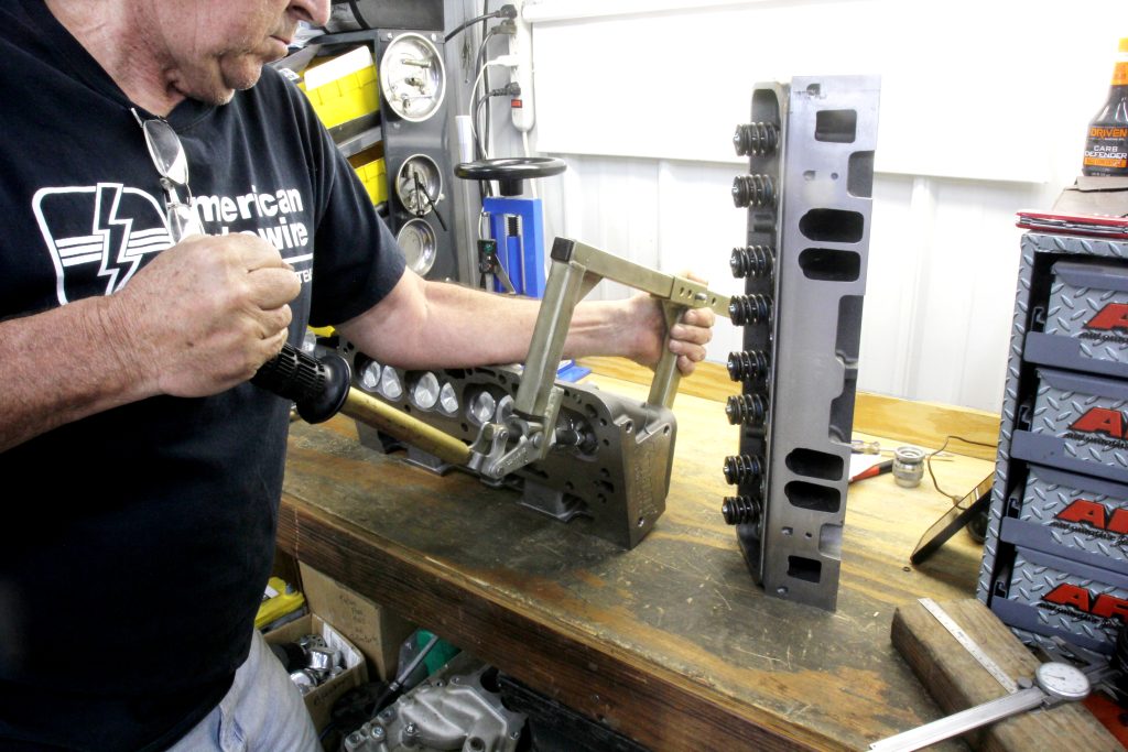 changing valve springs with a valve spring compressor tool on a workbench for a small block chevy v8 engine