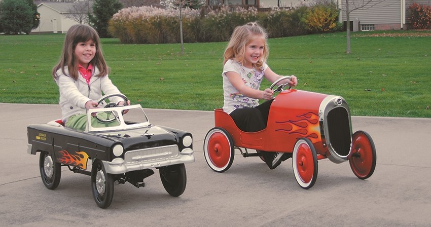 2 girls riding in 2 nostalgic metal pedal cars