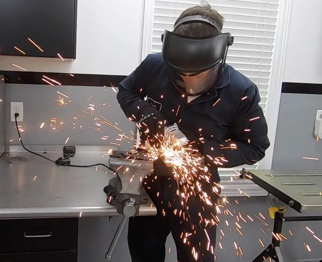 a man grinding metal clamped in a bench vise with sparks