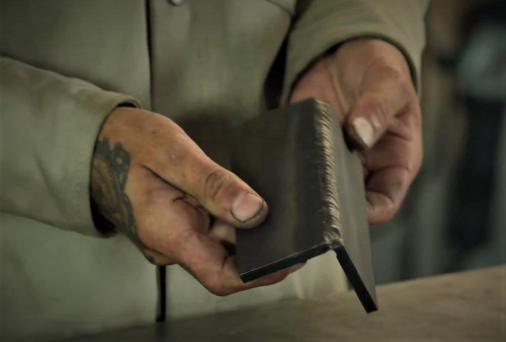 man holding a piece of steel that has been welded into a corner