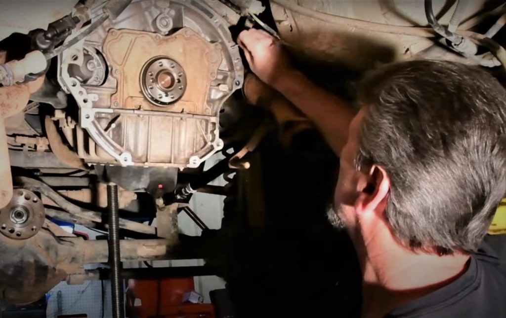 man cleaning bolt holes in a clutch bellhousing under a lift