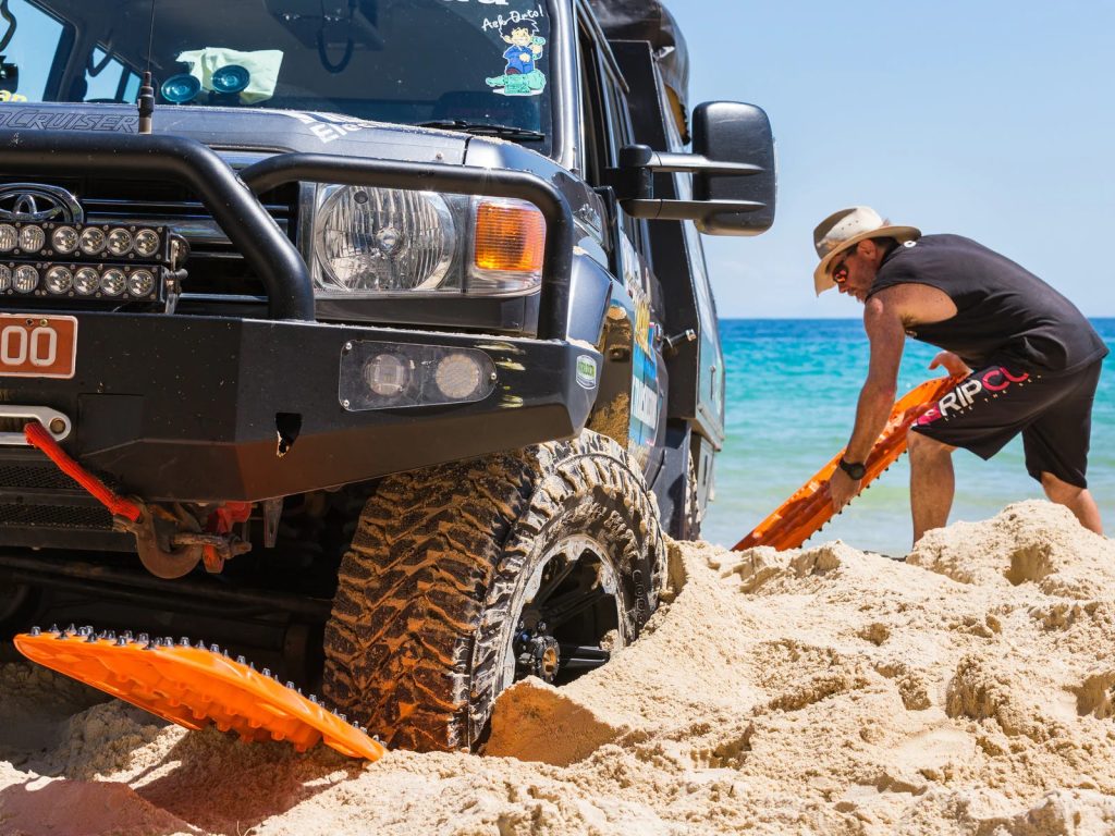 man fitting maxtrax recovery board set under wheels of a stuck truck off road