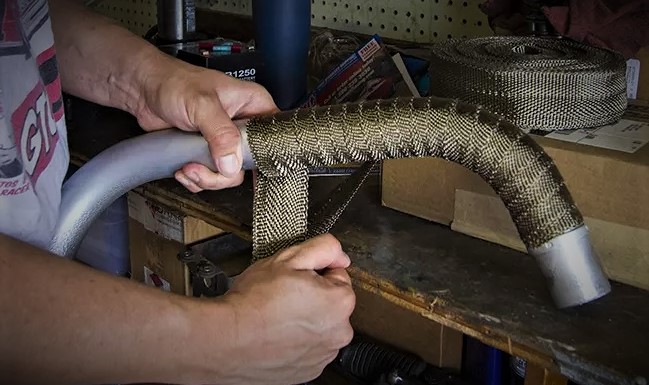 man wrapping a section of exhuast pipe in heat wrap covering