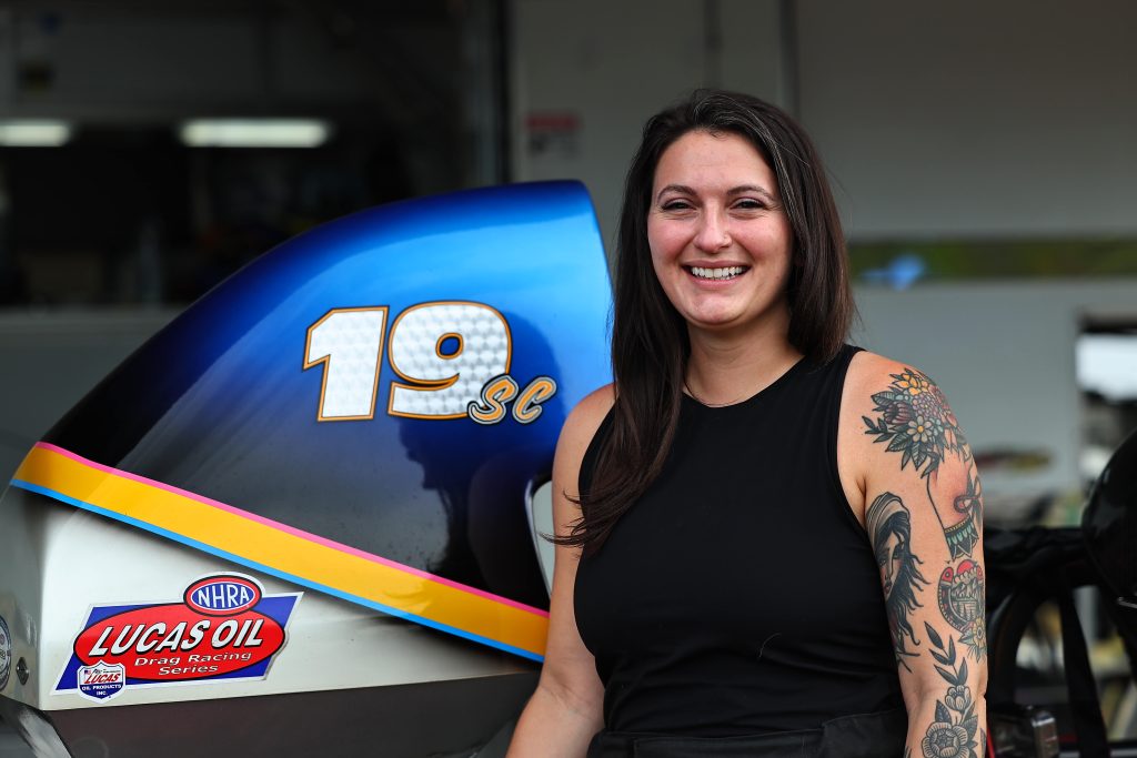 Smiling race car driver standing next to dragster