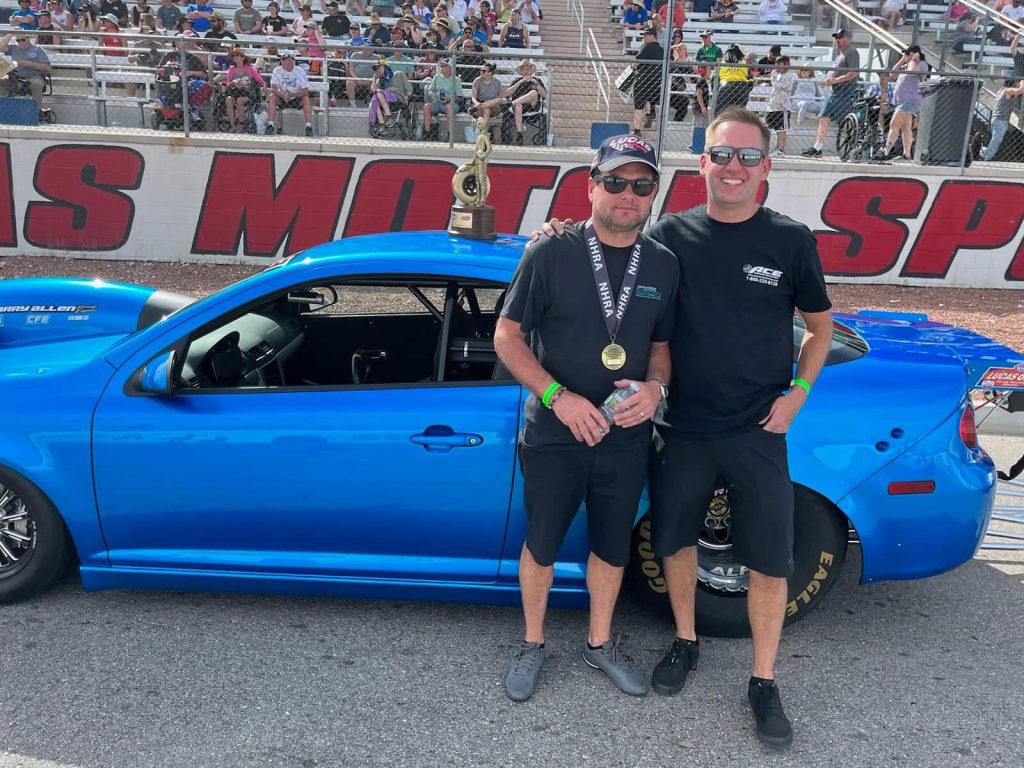 two men posing in front of a race car