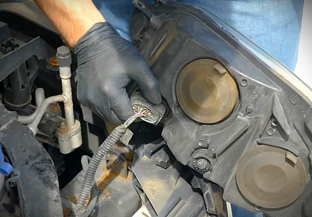man removing a headlight assembly from a car