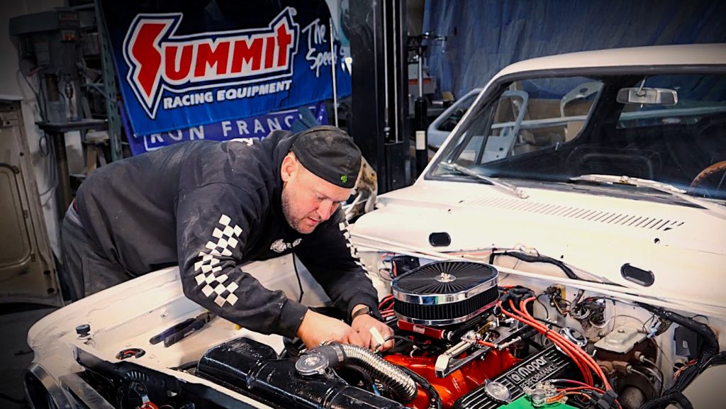 man installing wire harness in an engine bay